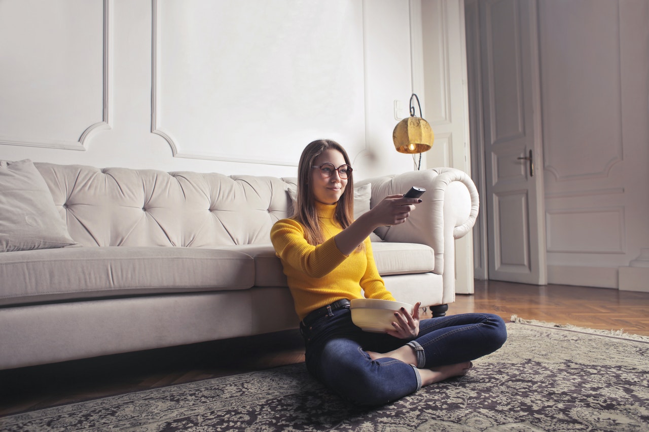woman sitting on the floor watching tv holding a bowl of popcorn