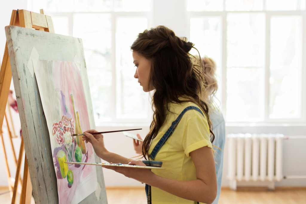woman painting in studio with easel and canvas at art class
